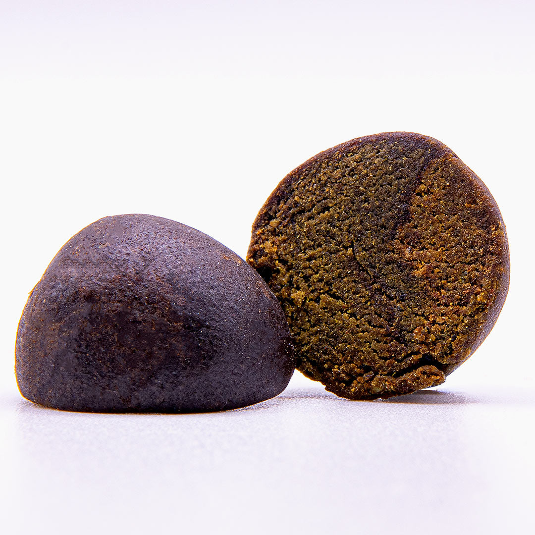 CBD Temple Ball Hash Kugel mit angeschnittener Hälfte und dunkelbrauner, feinkrümeliger Innenstruktur auf hellem Hintergrund