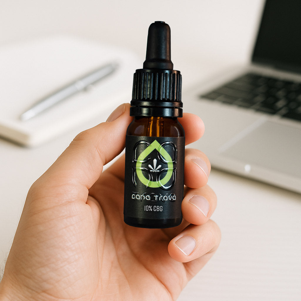 CBG Öl 10 % von Cana Trava in der Hand vor Laptop auf hellem Schreibtisch
